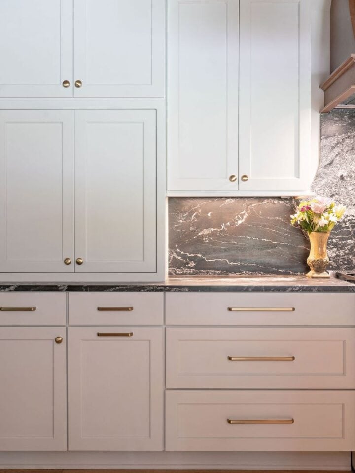 Elegant white kitchen cabinets with gold handles and marble backsplash.