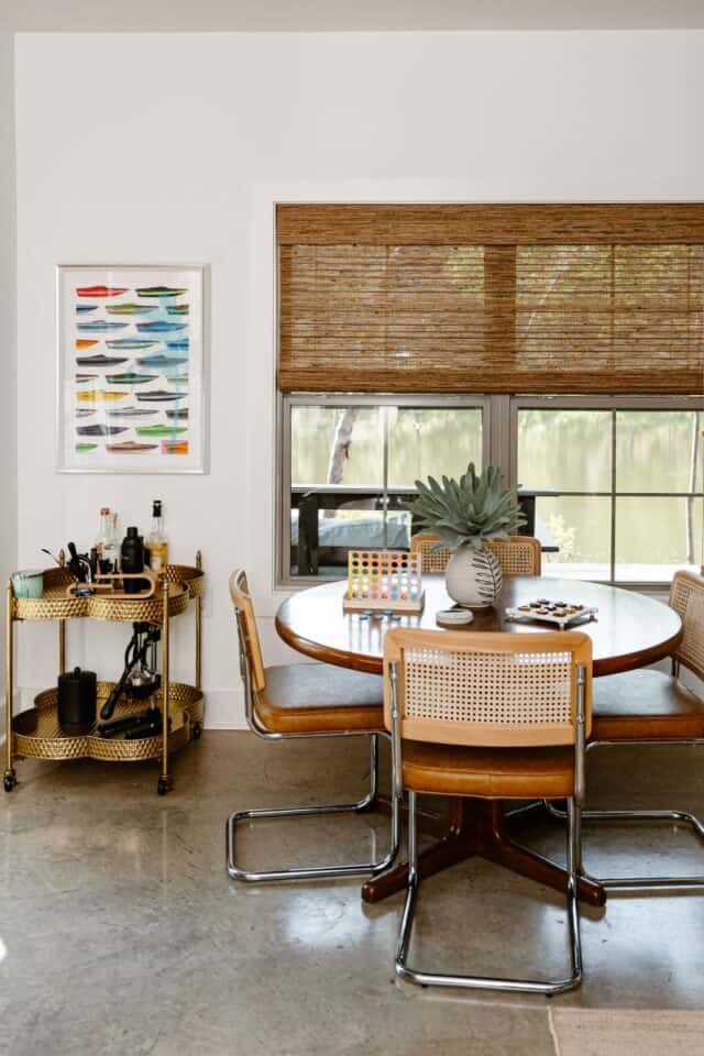 Contemporary dining area featuring a round table, rattan chairs, and a window with bamboo blinds.