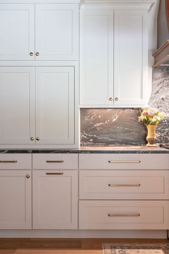 Modern white kitchen cabinets with gold hardware and marble backsplash.