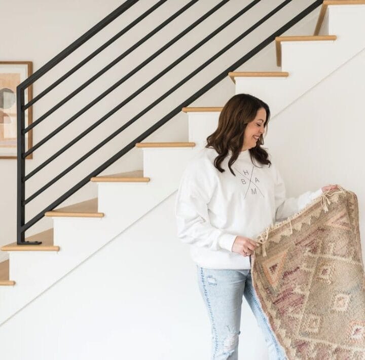 Woman holding Kristen McGee Interiors rug near staircase in modern home.