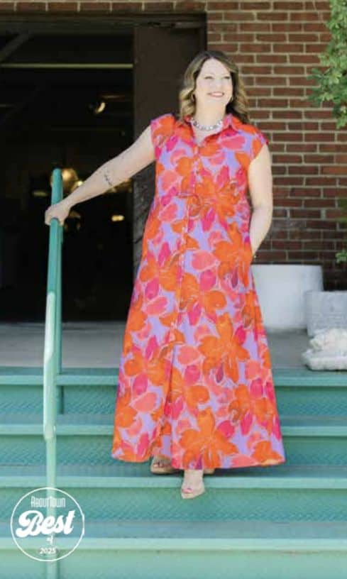 Woman in vibrant floral dress standing on stairs outside building.