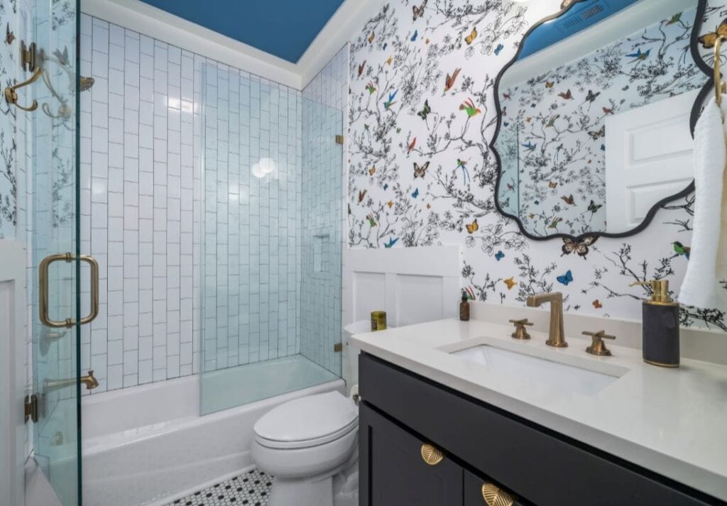 Modern bathroom with floral wallpaper, glass shower, and gold fixtures for elegant interior design.