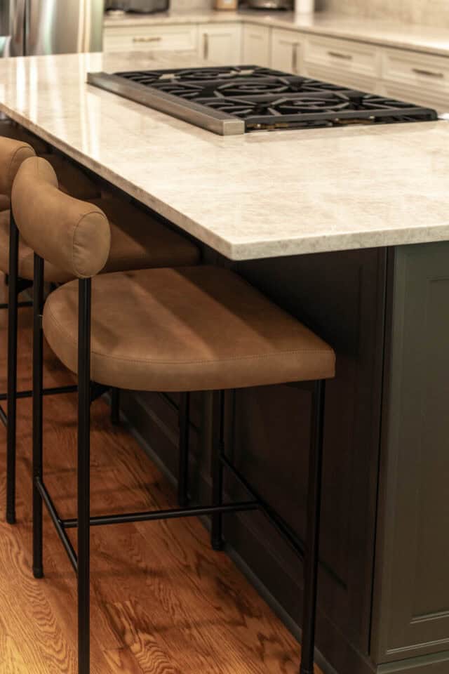 Contemporary kitchen island with beige bar stools and gas cooktop.