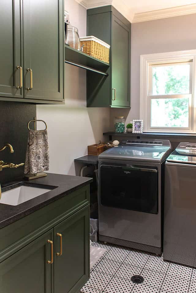 Stylish laundry room with green cabinets and black washer and dryer.