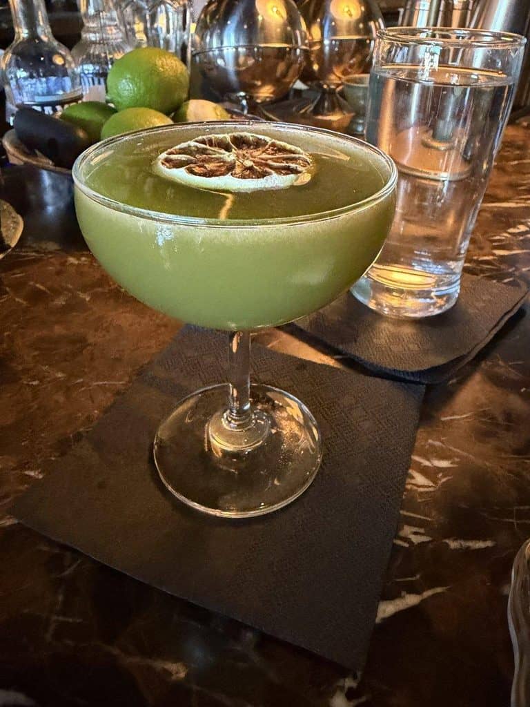 Refreshing green cocktail garnished with lemon slice on a dark bar table.
