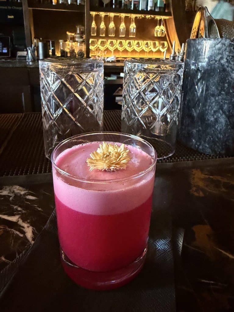 Vibrant pink cocktail with a flower garnish in a stylish bar setting.
