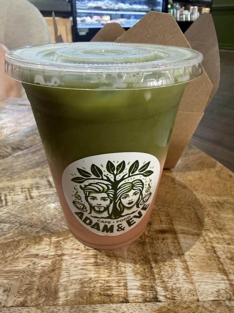Green matcha latte in clear cup with logo on wooden table.