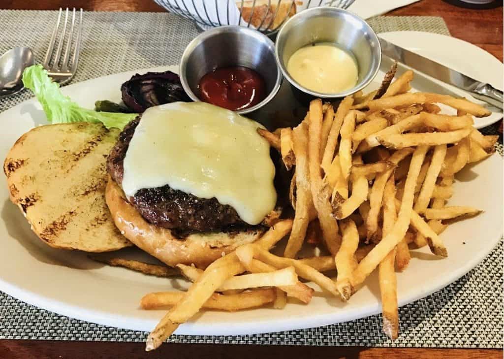 Juicy cheeseburger with melted cheese, fries, and condiments on a white plate.